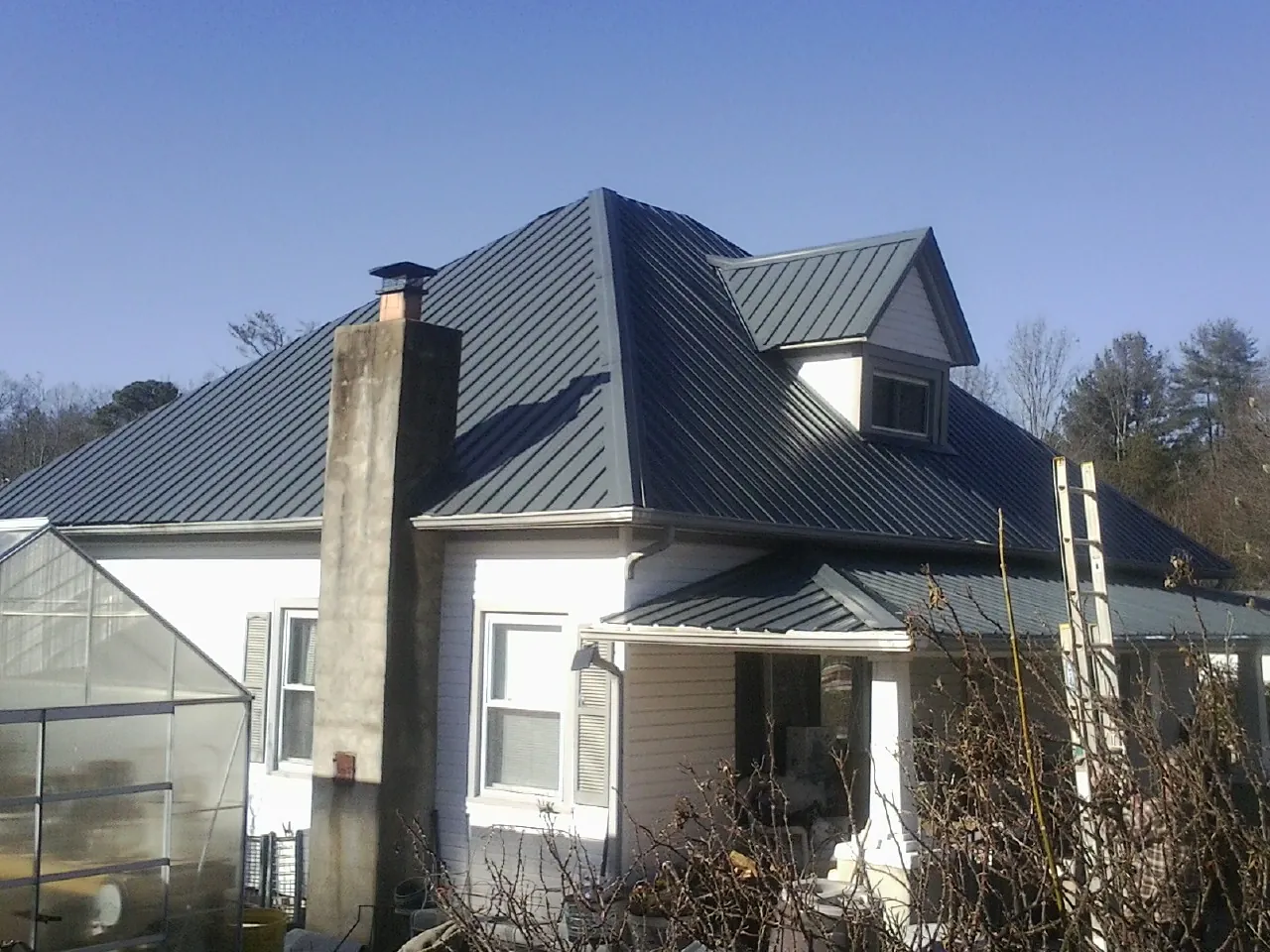 Dark blue standing seam metal roof on a white farmhouse with dormer — Slate & Tile Roof Repair by Roofing Brothers in Levels