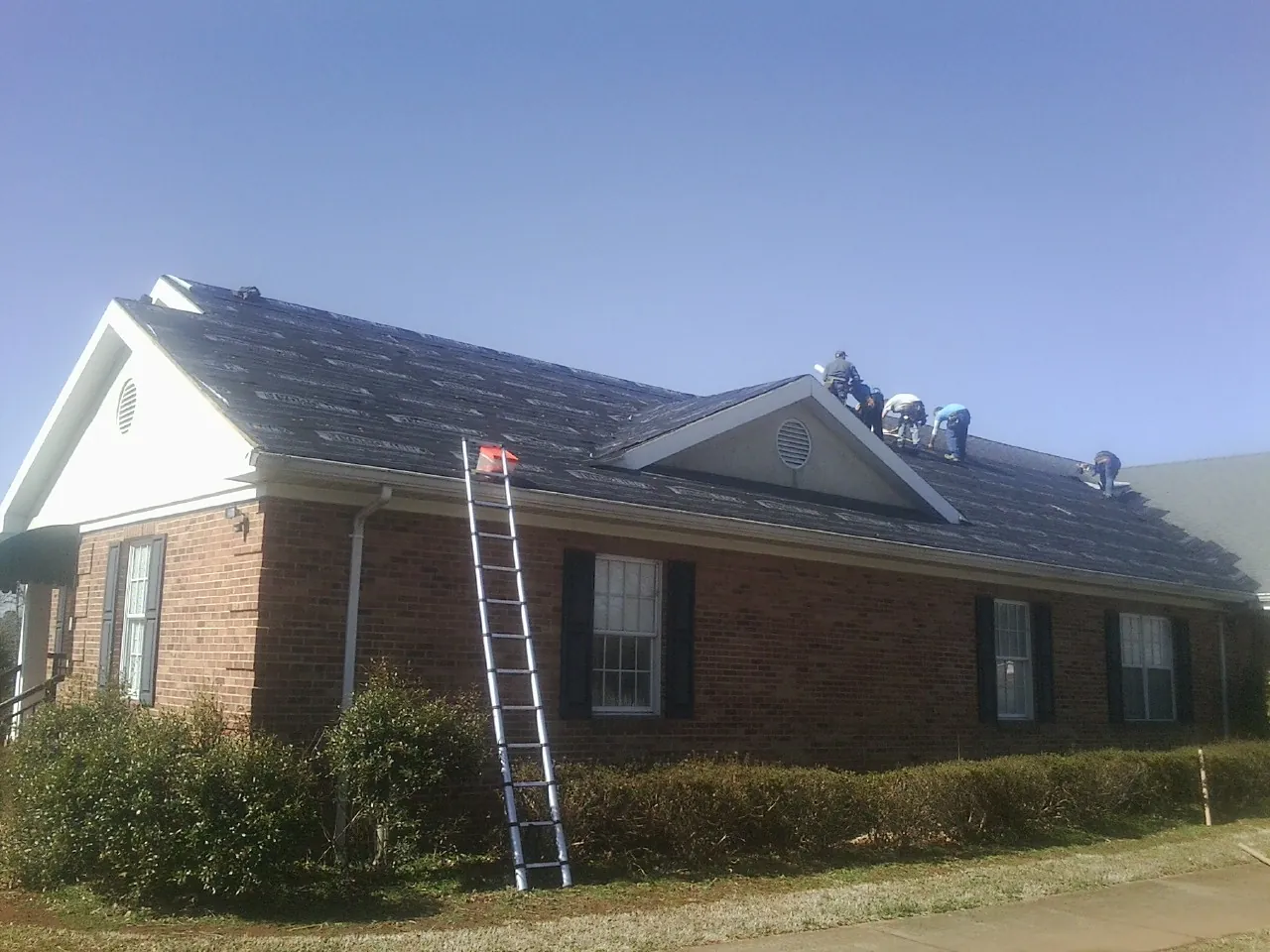 Crew tearing shingles off a brick ranch roof with a ladder set — Metal Roof Repair work by our crew in Levels