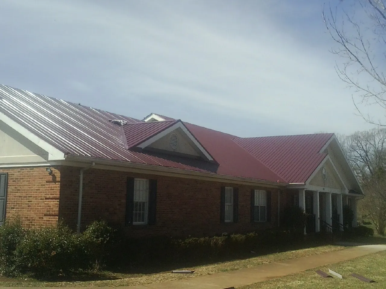 Red metal roof with gabled entries on a long brick building, from a Hail Damage Roof Repair job in Levels