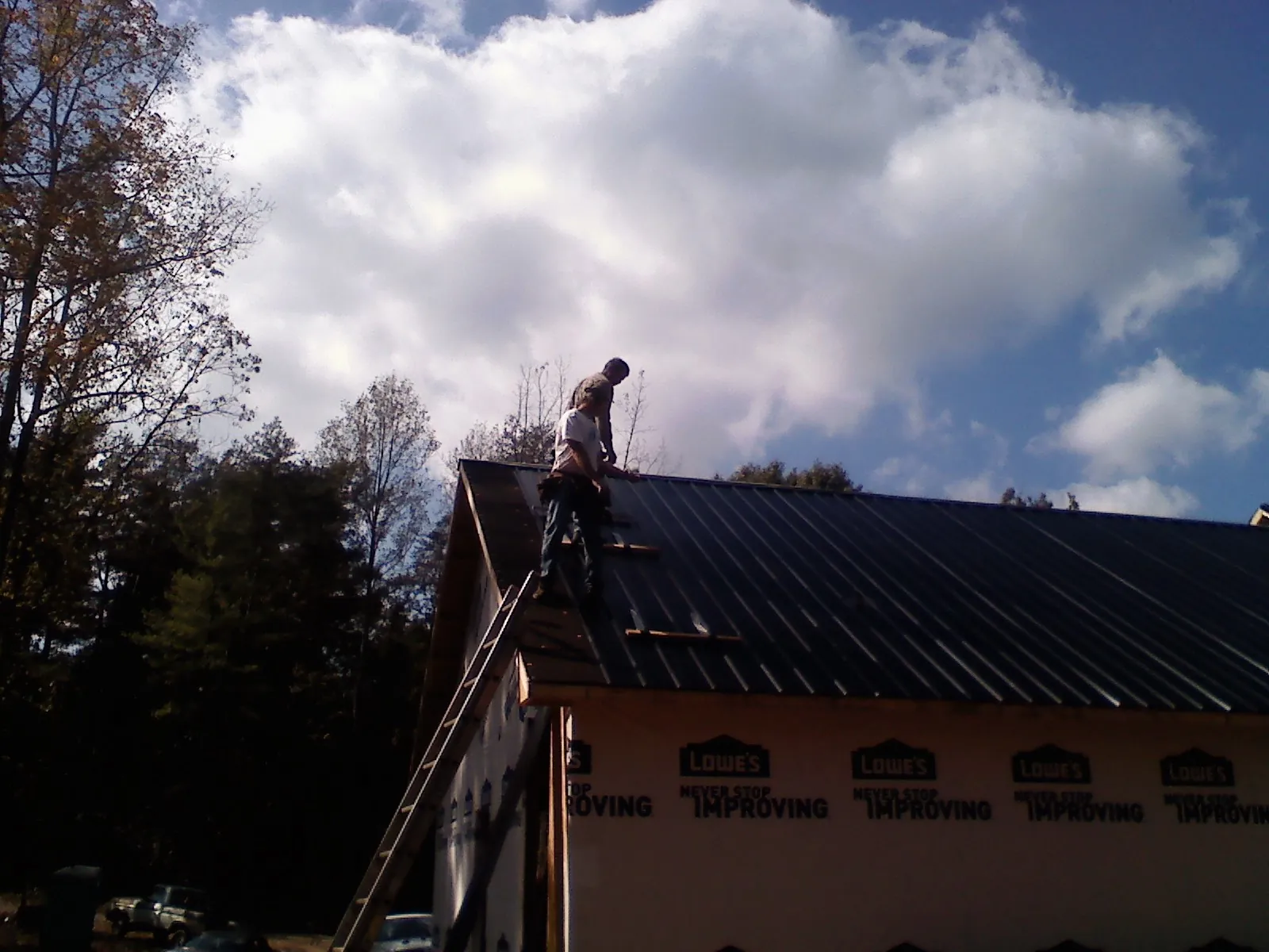 Roofer fastening dark metal panels high against a cloudy sky, from a Roof Inspection job in Levels