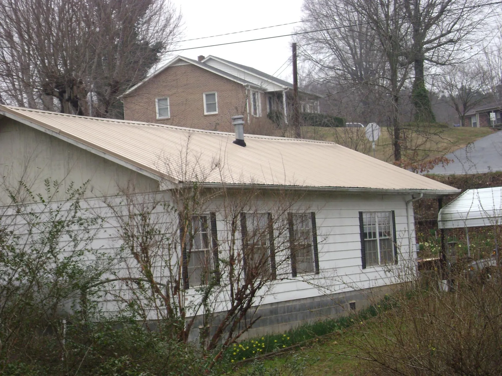 Tan metal roof on a white sided house set into a hillside — Commercial Roofing by Roofing Brothers in Levels