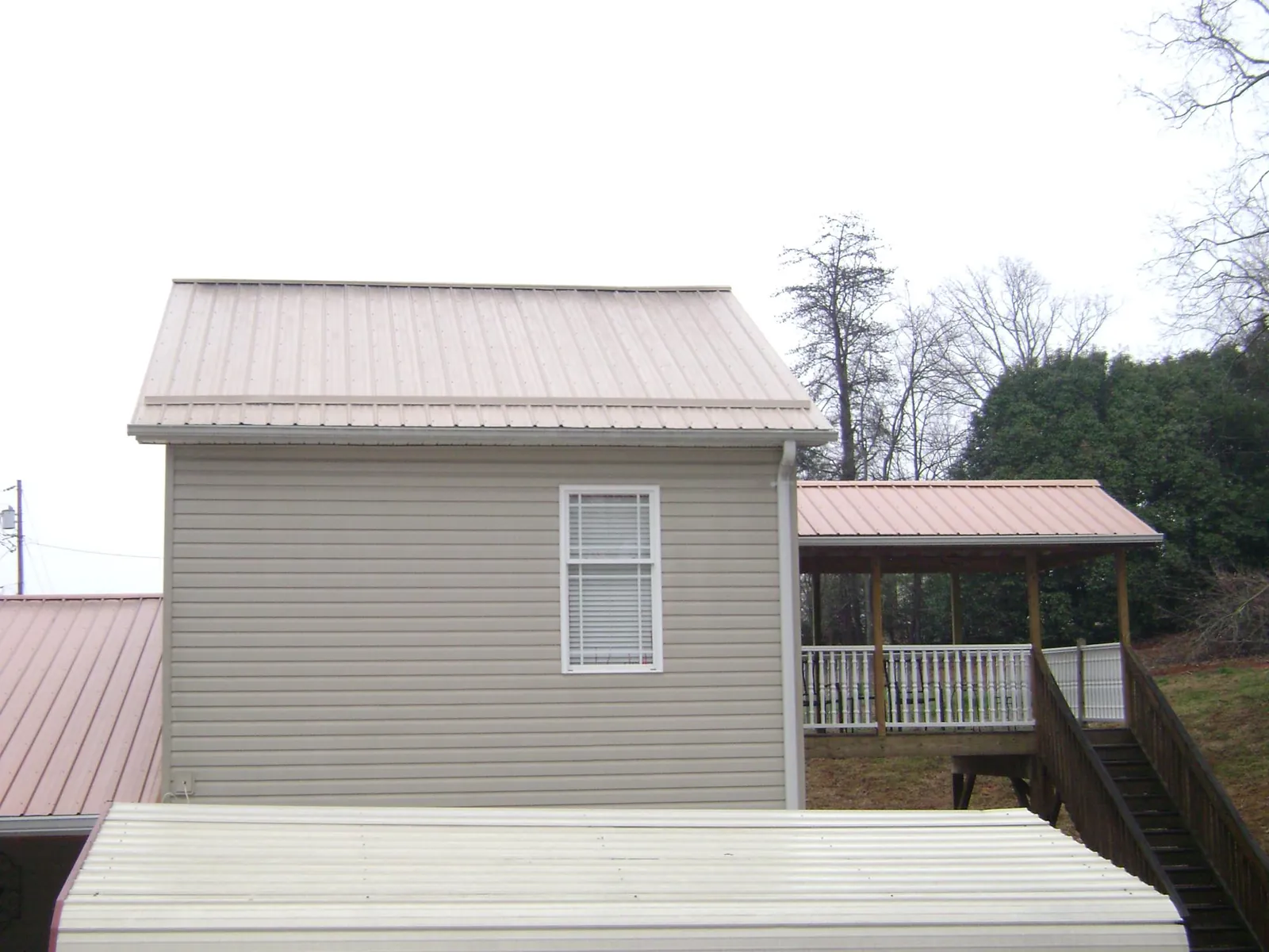 Tan metal roofs on a two story addition and attached porch, from a Roof Replacement job in Levels